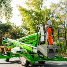 Worker on green aerial lift trimming trees